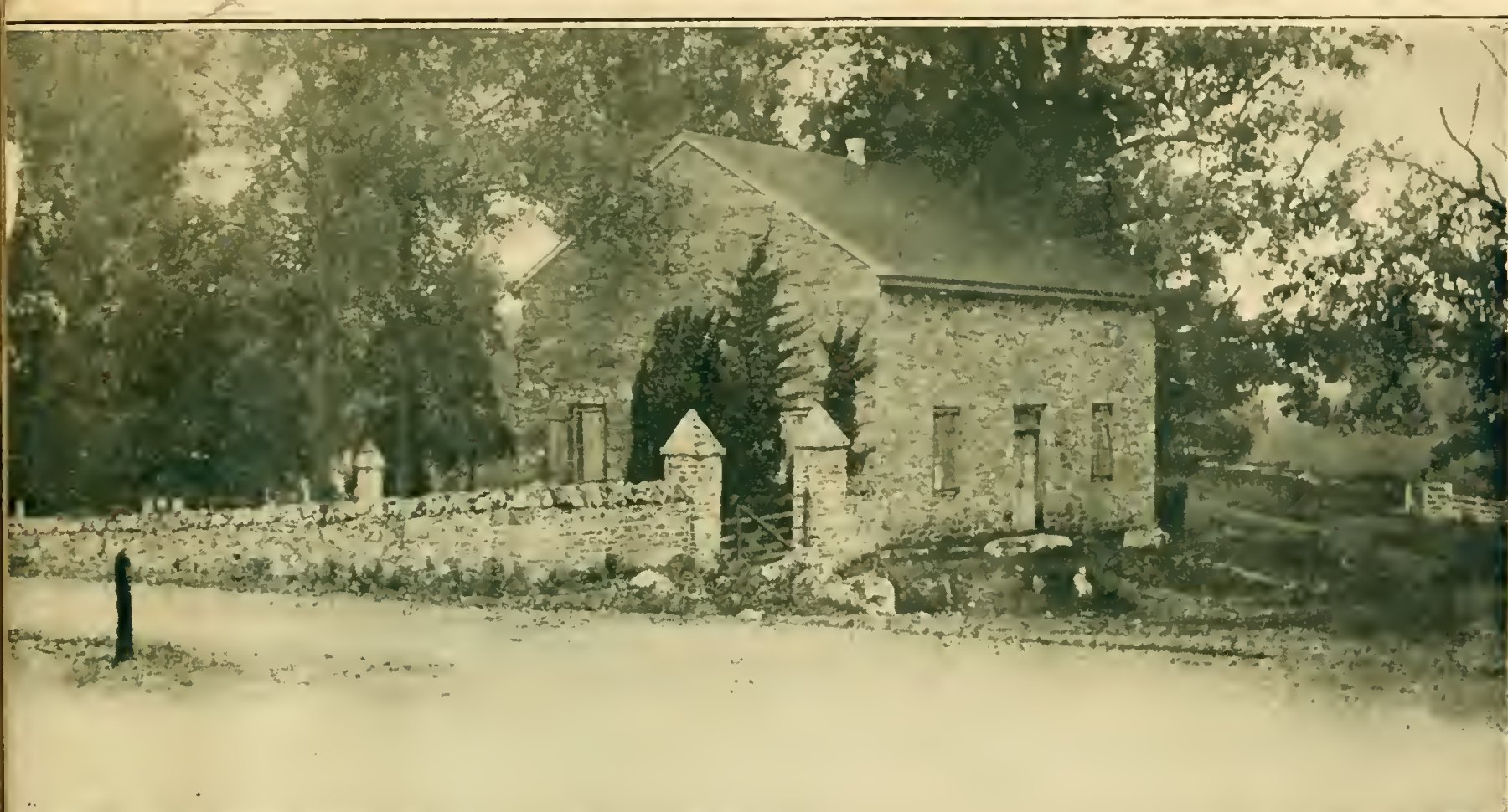 Old photograph of the Old Chapel, a stone church with a pitched roof among tall trees, behind a low stone wall with a gate between two stone posts.