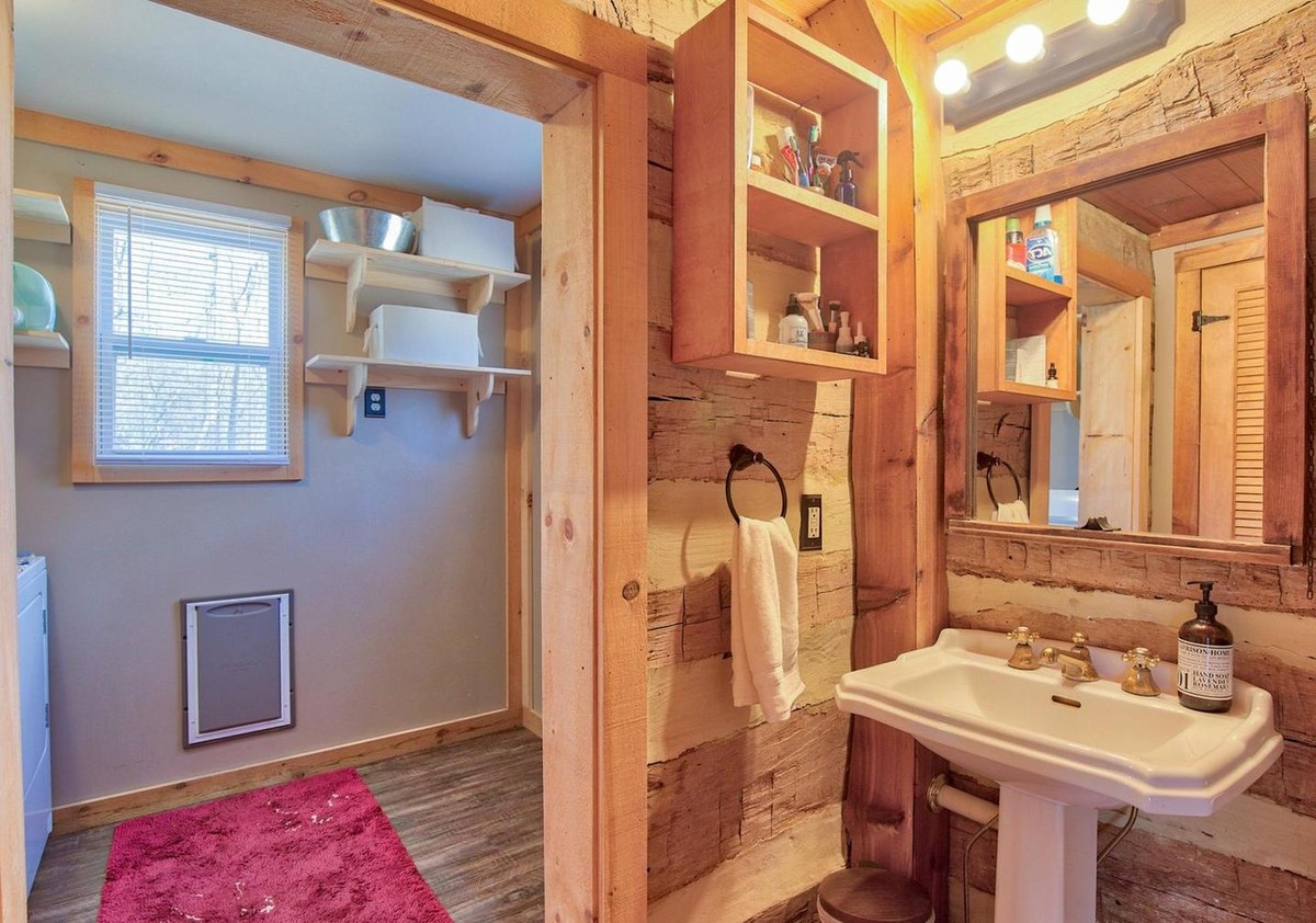 The bathroom sink close up, with a wall cabinet and mirror above, towels on hooks, and the laundry room visible through the doorway.