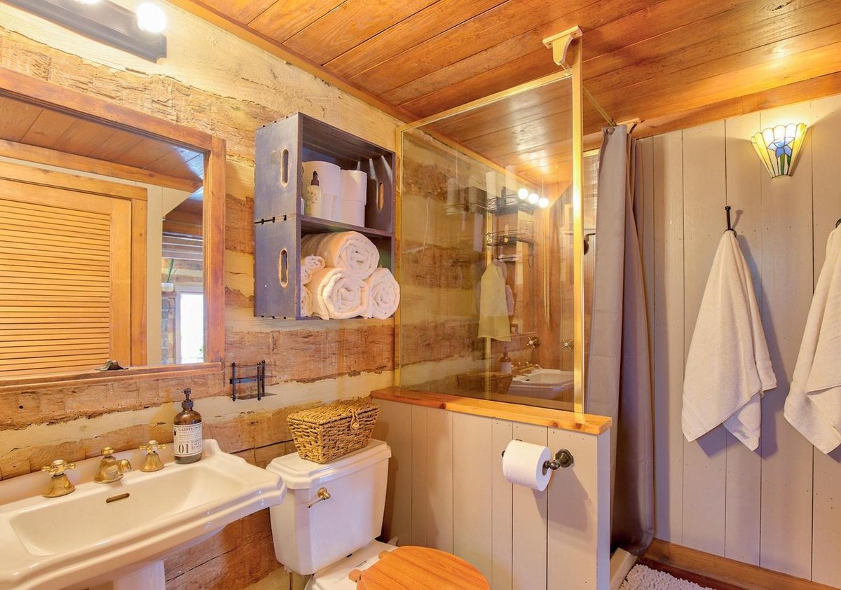 The bathroom from the other side: a louvered door, shelves of towels, the shower, towels on hooks and a small stained-glass lamp on the wall.