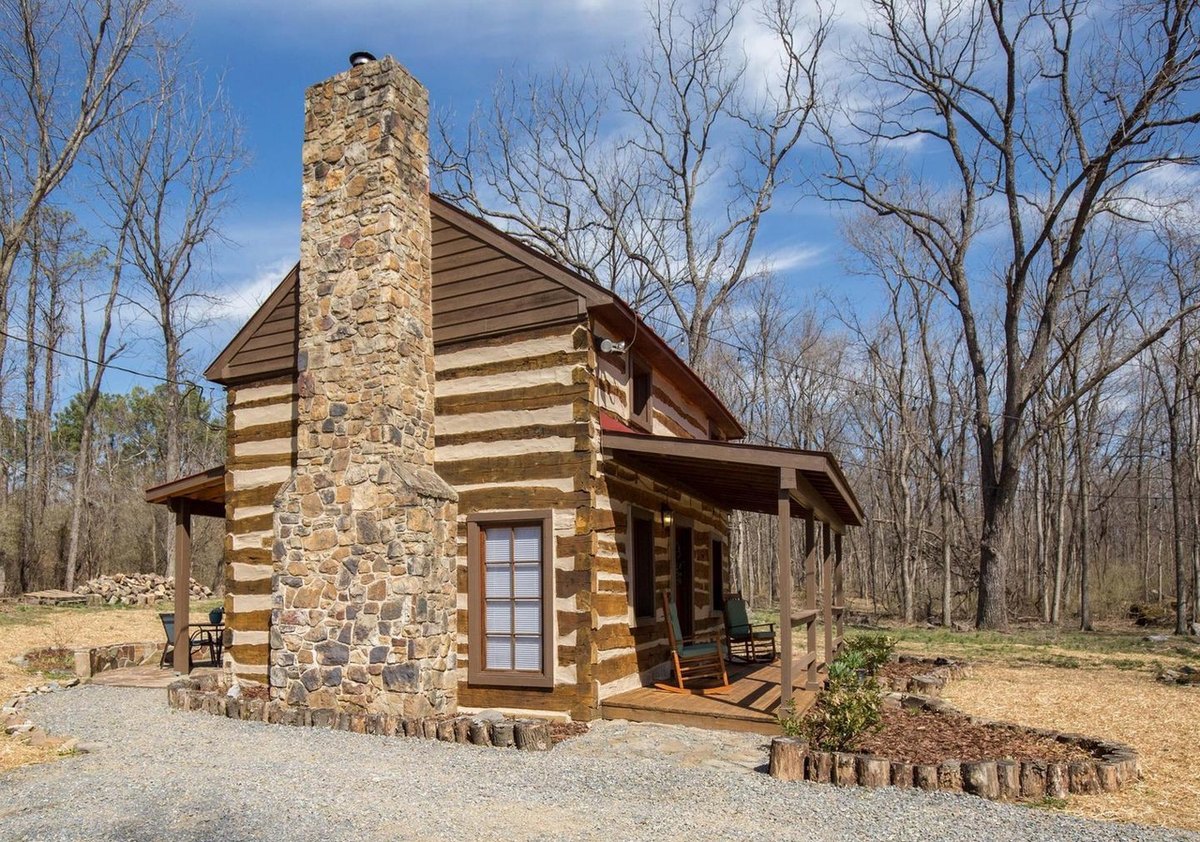 The chimney end of the cabin straight on: a fieldstone chimney with a glazed door beside it, the porch roof at the right and a gravel path curving past.