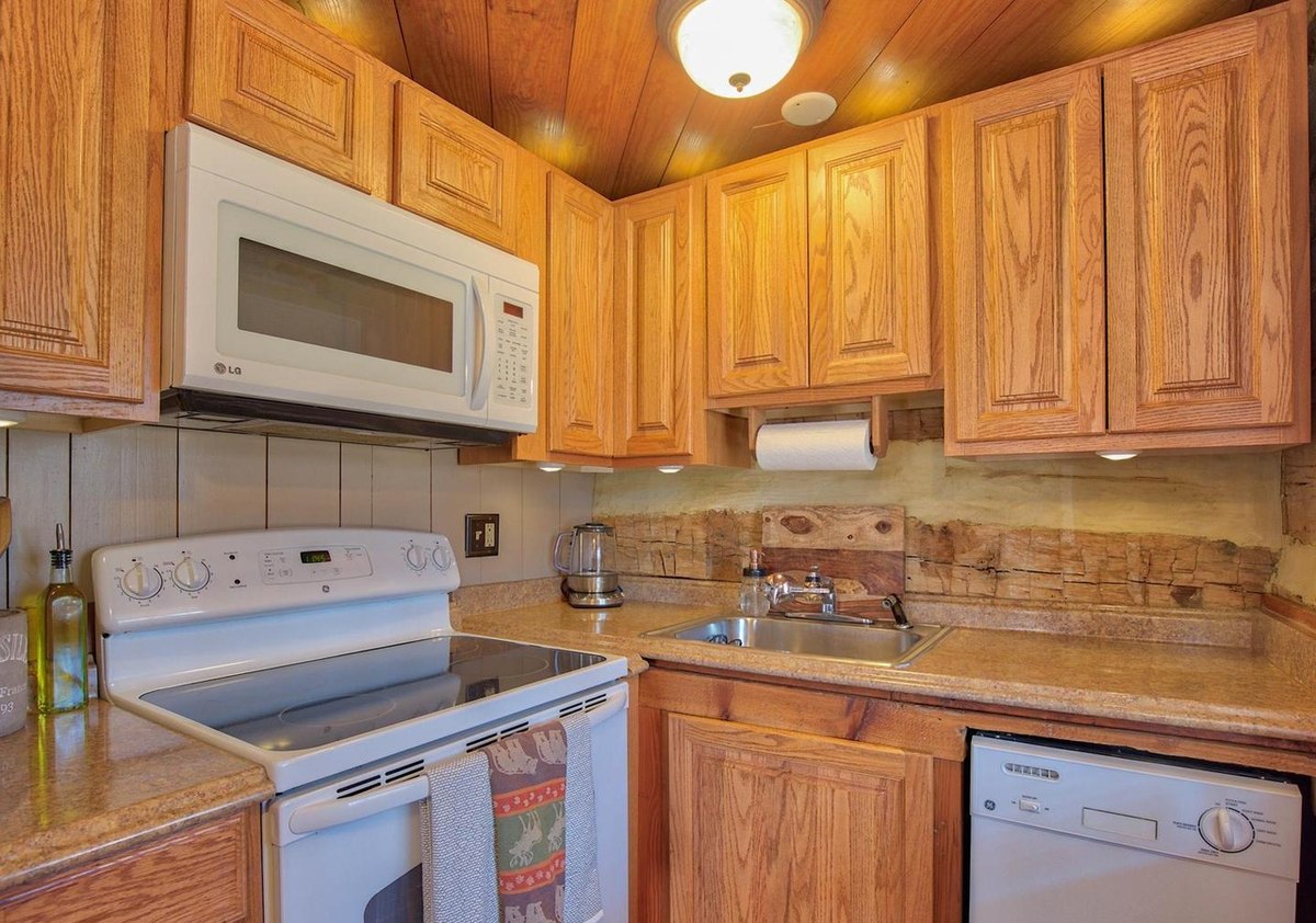 The kitchen close up: oak cabinets, a microwave over a white electric stove, a dishwasher, and a strip of hewn log wall behind the counter.