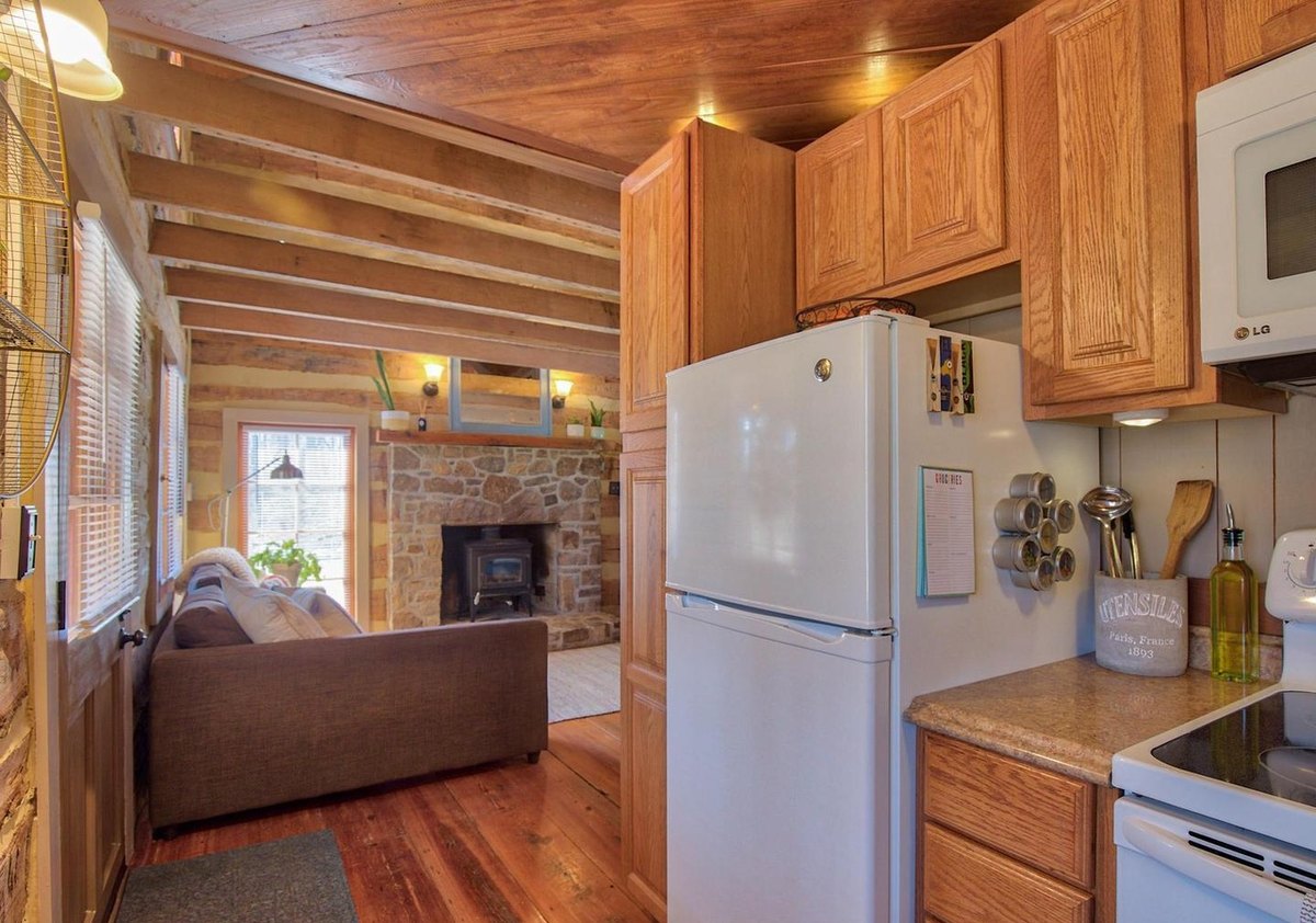 Looking from the kitchen past the refrigerator and cabinets into the main room, with the sofa and the stone fireplace beyond.