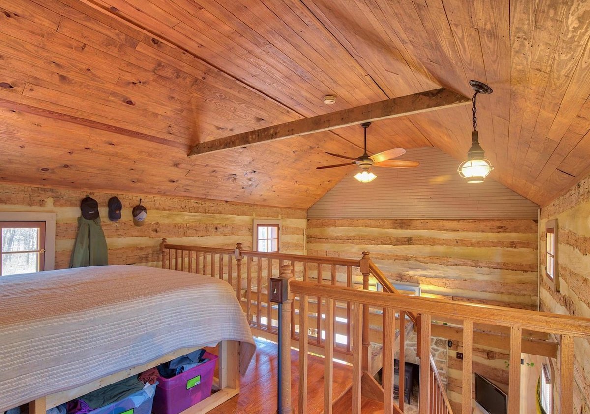 The upstairs room from beside the bed, looking across the stair railing under the sloping board ceiling with a fan and a hanging lantern.