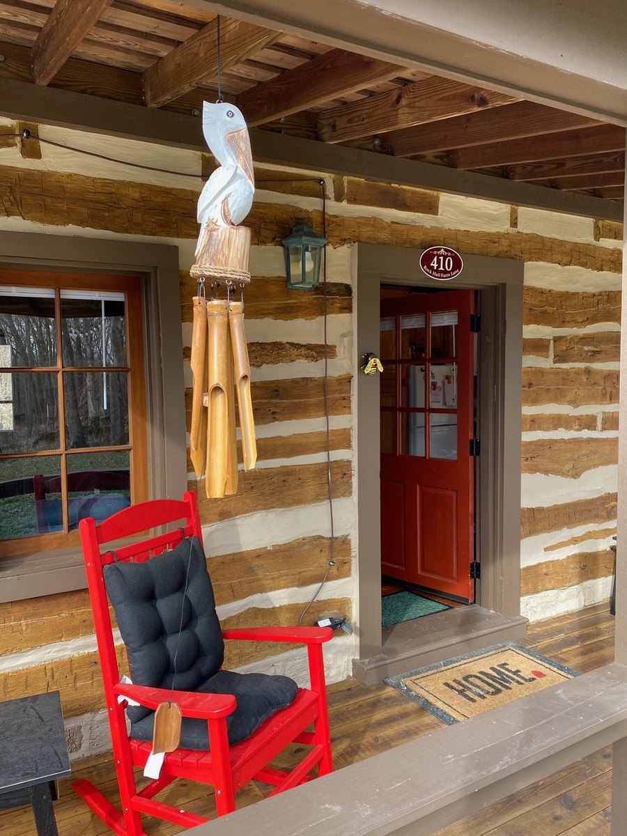 The front porch: a red rocking chair with a black cushion beside a window, a carved pelican wind chime hanging from the porch beams, and the open red front door with the 410 sign above it.